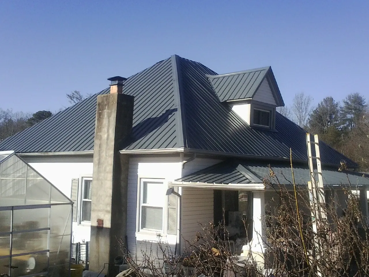 Dark blue standing seam metal roof on a white farmhouse with dormer — Slate & Tile Roof Repair by Roofing Brothers in Sandgap