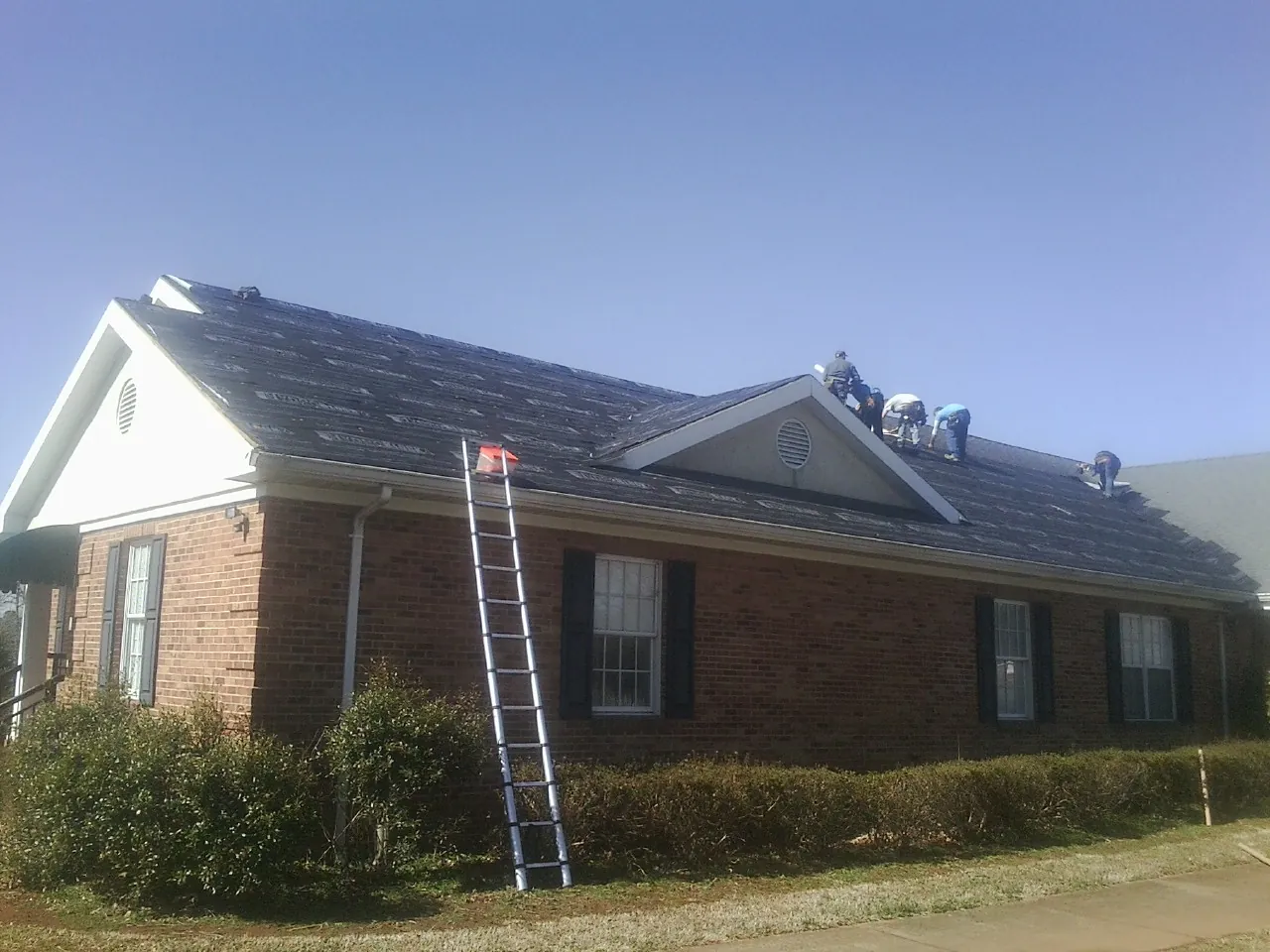 Crew tearing shingles off a brick ranch roof with a ladder set — Emergency Roof Repair work by our crew in Sandgap