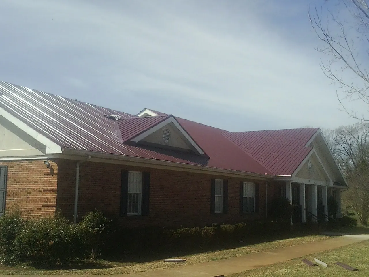 Red metal roof with gabled entries on a long brick building, from a Hail Damage Roof Repair job in Sandgap