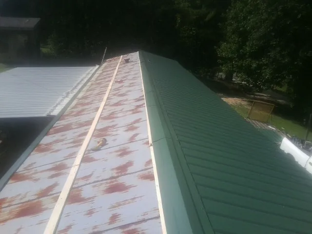 Old rusted panels beside newly installed green metal roofing — Wind Damage Roof Repair by Roofing Brothers in Sandgap