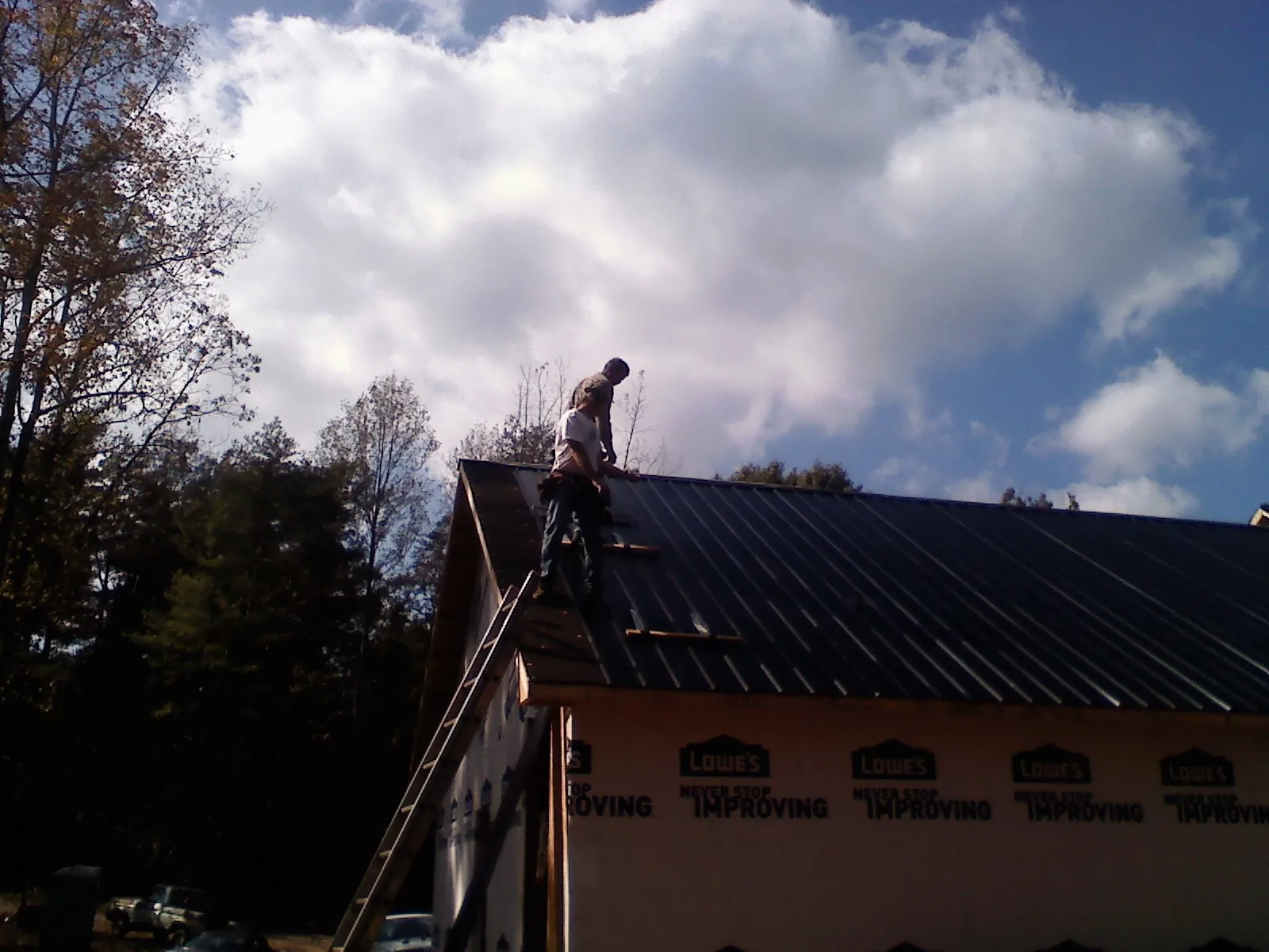 Roofer fastening dark metal panels high against a cloudy sky, from a Roof Inspection job in Sandgap
