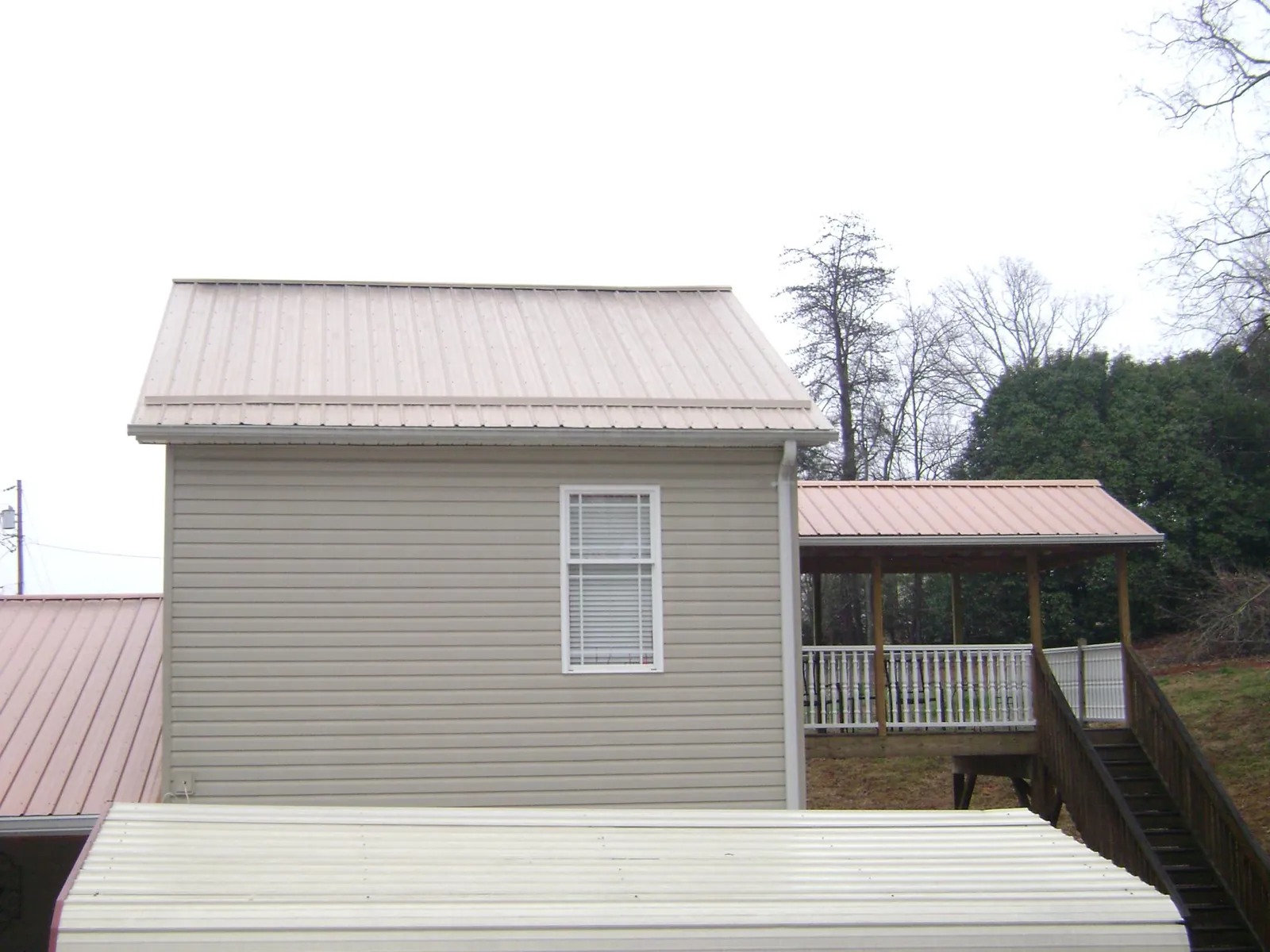 Tan metal roofs on a two story addition and attached porch, from a Roof Replacement job in Sandgap